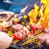 Brochettes et steaks sur un barbecue en feu. La conservation de la viande cuite au barbecue est essentielle pour profiter des restes.