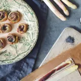 Petits roulés feuilletés à l'asperge blanche, parfaits pour un apéritif. Des asperges blanches, des graines de pavot et une touche de anchois complètent la scène.