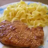 Une côte de porc savoureuse, nappée d'une sauce soja brillante et parsemée de graines de sésame, accompagnée de pâtes fraîches.