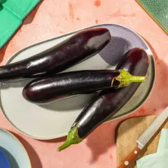 Trois aubergines allongées sur une assiette, prêtes pour des recettes d'été. Ces légumes de juin promettent de délicieux plats.