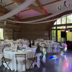 Salle de réception décorée pour un mariage de 80 personnes, tables dressées, lumières d'ambiance et DJ prêt à animer la soirée.