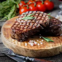 Deux steaks grillés sur une planche en bois, parsemés de gros sel rose. Une question se pose : quand saler la viande au barbecue pour un résultat parfait ?