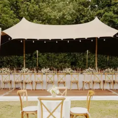 Une réception de mariage sous tente, avec des tables dressées et des chaises en bois. Un travail de cout wedding planner pour un événement mémorable.