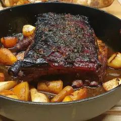 Poitrine de porc au four cuisson lente, dorée et savoureuse, accompagnée de pommes de terre rôties dans un plat en fonte.