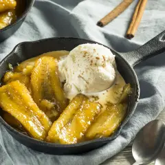 Bananes flambées au barbecue, servies chaudes dans une poêle en fonte avec une boule de glace à la vanille saupoudrée de cannelle.