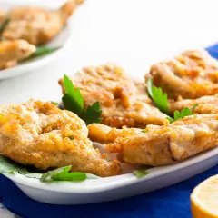 Délicieux artichaut frit, croustillant et doré, servi sur une assiette blanche avec des herbes fraîches et un quartier de citron.