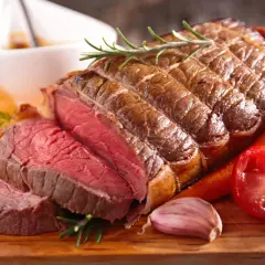 Un rôti de bœuf de 1k500, saignant et savoureux, servi avec des carottes, une tomate et de l'ail. Le temps de cuisson parfait pour ce délice.
