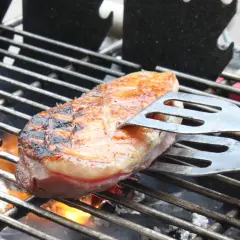 Une aiguillette de canard au barbecue, saisie à la perfection, avec des marques de grill et une peau dorée. Les pinces à barbecue maintiennent la viande sur la grille chaude.