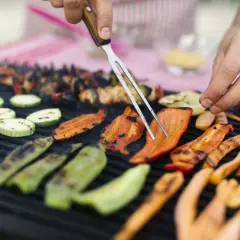 Des légumes accompagnement barbecue grillent sur le feu : courgettes, poivrons et carottes. Un homme les retourne avec une fourchette.