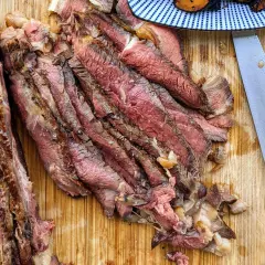 Tranches de bœuf juteuses, parfaitement cuites par la méthode du reverse searing, sur une planche en bois. Un couteau est à côté.