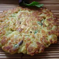 Une galette de pois cassés dorée et croustillante, garnie de persil frais, repose sur un tapis de bambou.