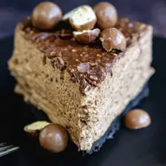 Une part de gâteau au chocolat aérien, garnie de boules Malteser croquantes et d'un glaçage au chocolat.