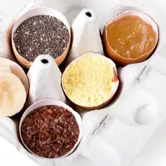 Dans une boîte à œufs, des alternatives pour remplacer les œufs : graines de chia, compote de pommes, farine de pois chiche, graines de lin, rondelles de banane.