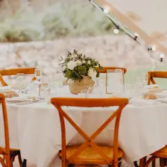 Table dressée pour un repas traditionnel mariage français, avec des chaises en bois, des fleurs et des petits pains.