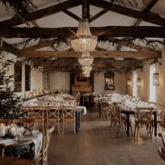 Une salle de réception décorée pour un mariage en hiver, avec un sapin illuminé, des guirlandes lumineuses et des tables dressées.