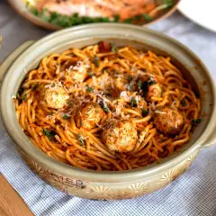 Spaghetti aux boulettes de viande dans un plat en céramique, parsemé de parmesan et d'herbes. Une recette facile et gourmande parfaite pour un repas convivial.