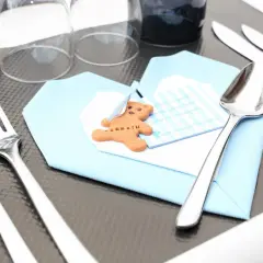 Un biscuit en forme d'ours sur une serviette bleue, prêt pour un baptême. Le tableau budget baptême est bien organisé.