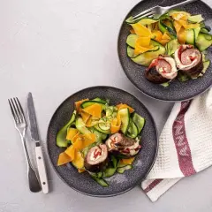 Deux assiettes de involtini, roulés de viande farcis, servis avec une salade de courgettes et carottes en rubans.