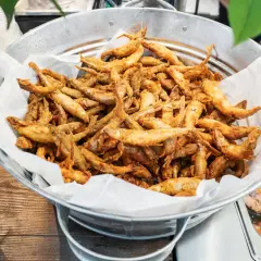Un seau rempli d'éperlans frits dorés, prêts à être dégustés. Ces petits poissons croustillants sont un délice.