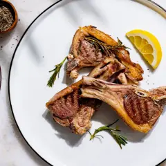 Trois côtelettes d'agneau grillées, garnies de romarin et de citron, prêtes pour le temps de cuisson idéal.
