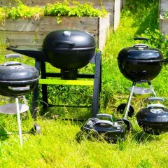 Plusieurs barbecues, certains à charbon, d'autres à bois, sont prêts pour un festin estival dans l'herbe verte.