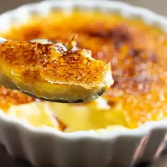 Une cuillère soulève une bouchée de crème brûlée clementine, révélant sa croûte caramélisée craquante et sa crème onctueuse.