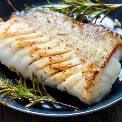 Un filet de poisson blanc parfaitement cuit, peau dorée et chair nacrée, servi avec du romarin frais. Une belle illustration de comment cuire du poisson blanc.