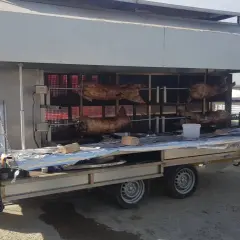 Remorque tourne broche fait maison avec plusieurs carcasses de viande en cuisson. Une marmite et une bouteille de gaz sont visibles sur le côté.