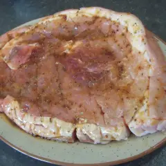 Rouelle de porc prête pour la plancha, généreusement recouverte d'une marinade savoureuse aux herbes et épices.