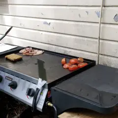 Un barbecue avec une bouteille de gaz prépare un petit-déjeuner savoureux : saucisses, bacon et tomates grillées.
