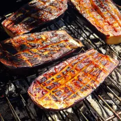 Aubergines coupées en deux, grillées au barbecue, avec des marques de cuisson caramélisées et une chair tendre.