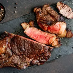 Un steak de bœuf juteux, coupé en tranches, révèle une cuisson parfaite grâce à la méthode de cuisson reverse sear. Poivre noir et blanc en accompagnement.