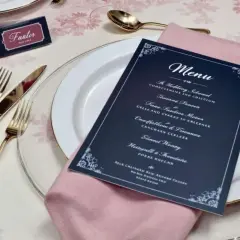 Une table dressée pour un mariage, avec une carte de menu originale, des couverts dorés et une serviette rose.