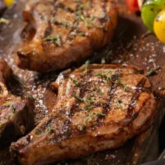Trois côtelettes de porc grillées, garnies d'herbes et de gros sel, sur une planche en bois. Une surprise de porc barbecue prête à être dégustée.