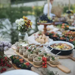 Un buffet baptême chic en extérieur, avec des verrines, des plats chauds et des décorations naturelles comme de l'ail et des tomates.