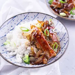 Délicieux accompagnement travers de porc laqué, servi avec du riz blanc et garni d'oignons caramélisés et de ciboule.