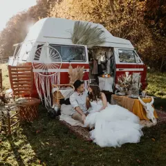 Un couple en tenue de mariage profite d'un mariage pique-nique champêtre près d'un van aménagé, décoré de style bohème.