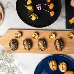 Assortiment de bouchées variées, parfaites pour un manger froid. Mini-burgers, tartes salées et sandwichs au saumon sur planche en bois.
