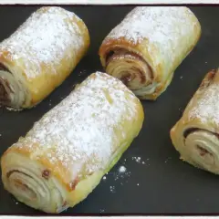 Quatre croissants au chocolat en pâte feuilletée, saupoudrés de sucre glace, prêts à être dégustés.