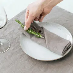 Une main dépose une branche de romarin sur un pliage de serviette mariage, sur une assiette blanche.