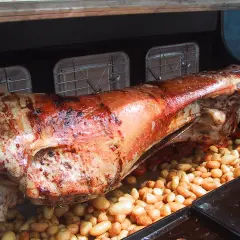 Gigot à la broche doré et juteux, rôti lentement avec des pommes de terre et des tomates cerises en dessous.