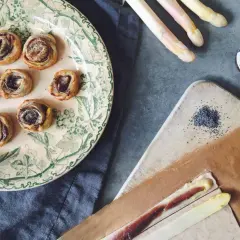 Petits roulés feuilletés à l'asperge blanche, parfaits pour un apéritif. Des asperges blanches, des graines de pavot et une touche de anchois complètent la scène.