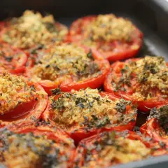 Tomates au barbecue, coupées en deux et garnies d'une chapelure dorée et d'herbes aromatiques, prêtes à être dégustées.