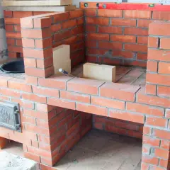 Construction d'un barbecue fait maison en briques rouges. Des briques supplémentaires et un niveau à bulle sont visibles sur le chantier.