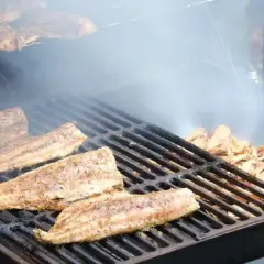 Poisson fumé sur un gril, avec des copeaux de bois qui dégagent de la fumée. Idéal pour savoir quel bois pour fabriquer un fumoir.