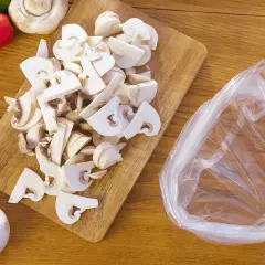 Champignons frais coupés sur une planche en bois, prêts à être mis dans un sac pour apprendre comment congeler des champignons frais.