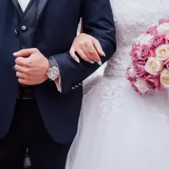 Un couple uni, main dans la main, bouquet de roses roses et blanches. Vive les mariés !
