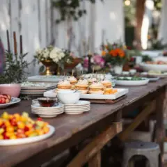 Buffet mariage bohème chic : petits fours, salades de fruits colorées et fleurs champêtres sur une table en bois rustique.