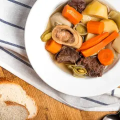 Un réconfortant pot-au-feu d'hiver avec du bœuf, des carottes, des poireaux et une os à moelle, servi avec du pain croustillant.