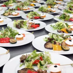 Organisation buffet : assiettes individuelles de salade fraîche, légumes grillés et amuse-bouches joliment dressés, prêts à être servis.